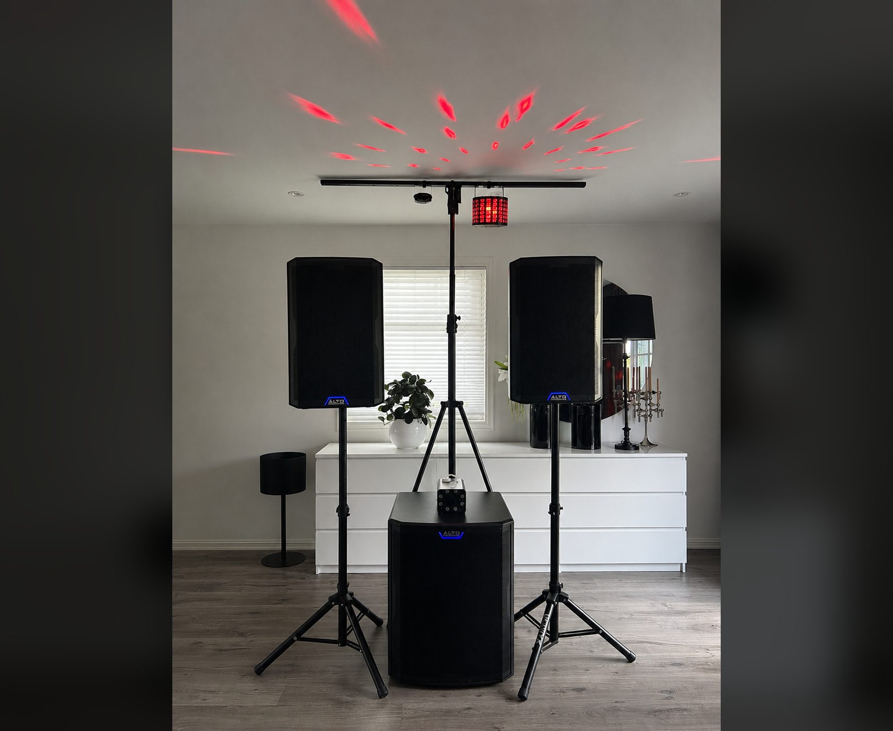 FestRiggen i stue: to høyttalere på stativ, subwoofer og lysbom som kaster røde mønstre i taket